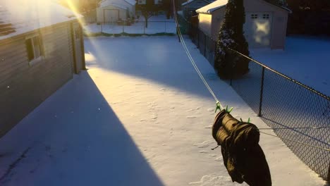 Wide-time-lapse-of-sun-setting-from-light-to-dark,-throwing-a-moving-shadow-on-a-snowy-backyard,-with-jacket-hanging-on-a-laundry-line,-swinging-wildly-in-the-high-winds