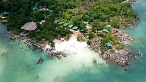 Aerial-reveal-of-a-private-island-paradise-beach-resort-with-wooden-beach-huts-in-Koh-Rong-Sanloem,-Cambodia