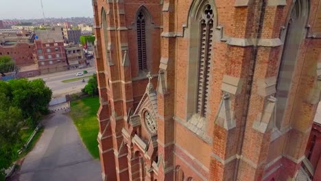 Close-up-aerial-view-of-A-beautiful-old-Church,-A-cross-on-the-Church-building,-Traffic-is-moving-on-the-other-side-road-of-the-Church