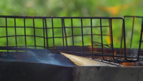 Burning-wood-an-coals-in-rusty-portable-outdoor-BBQ-grill-in-sunny-day,-close-up-shot