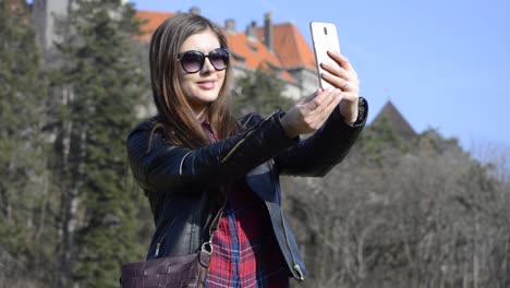 Pretty-young-brunette-girl-with-sunglasses-taking-selfies-with-a-castle-in-a-public-park