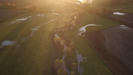 Aerial-view-of-a-commuter-train-passing-through-a-English-landscape-over-the-river-Stour-with-a-beautiful-sunrise-glow