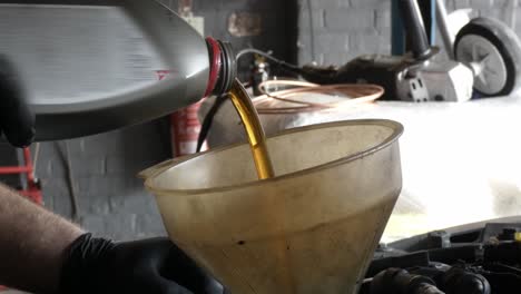 Pouring-new-oil-into-car-engine-from-a-bottle-using-a-dirty-funnal-in-a-garage