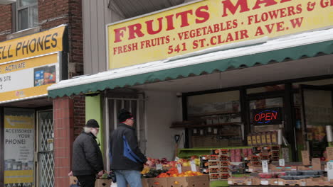 Driving-past-an-open-fruit-market-on-with-two-customers-looking-at-produce-outside