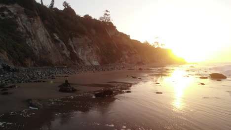 A-man-sitting-in-peaceful-meditation-and-present-awareness-on-a-sandy-beach-with-ocean-waves-at-sunrise-in-Santa-Barbara,-California-AERIAL-DRONE