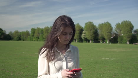 Happy-smiling-gorgeous-italian-girl-enjoying-walking-around-the-park-while-typing-text-via-smartphone-gadget,-positive-female-tourist-using-technology-to-communicate