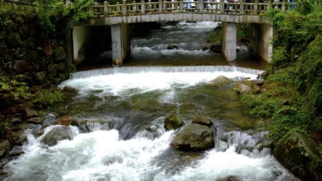 Mountain-stream-coming-down-past-mossy-rocks---under-Korean-bridge