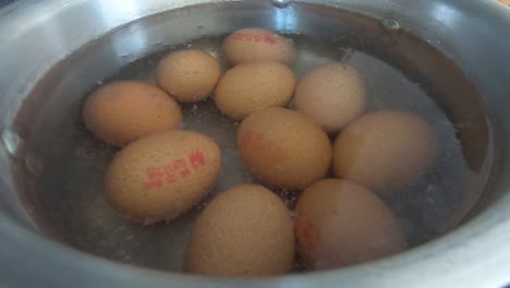 Close-up-of-10-eggs-slowly-coming-to-boil-in-water-in-a-silver-pot-pan-in-a-kitchen