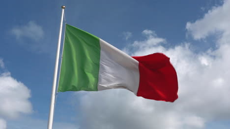Ondeando-Una-Bandera-Italiana-Verde,-Blanca-Y-Roja-Casi-Recta-Con-Un-Fuerte-Viento-Con-Un-Cielo-Azul-Real-Y-Nubes-En-El-Fondo