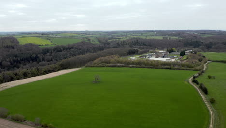 Aerial-Flyover-Shot-of-Field-and-Tree-with-Industry-Visible-in-Yorkshire,-England-during-a-Cloudy-Spring-Day