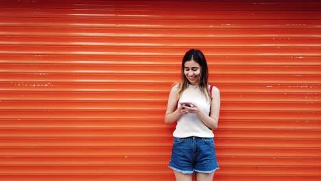 Schönes-Junges-Mädchen-Nutzt-Smartphone-Vor-Orangefarbenem,-Rotem-Hintergrund
