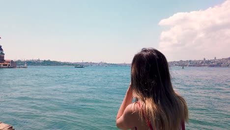 Beautiful-girl-takes-pictures-of-Bosphorus-and-Maidens-Tower-in-Uskudar-town,Istanbul,Turkey