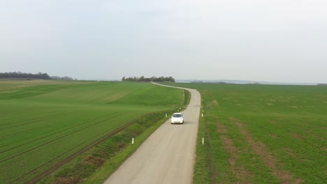 White-car-driving-towards-viewer-on-country-road-through-Lower-Austria,-aerial-view-from-drone-flight