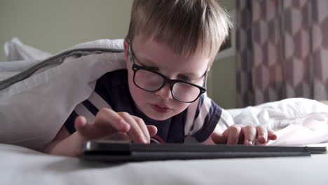 A-six-years-old-boy-reading-a-computer-tablet-while-lying-in-his-bed