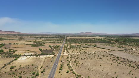 High-flying-aerial-video-of-a-Mexican-highway-with-traffic-in-the-desert-with-blue-skies-and-mountains-in-the-background