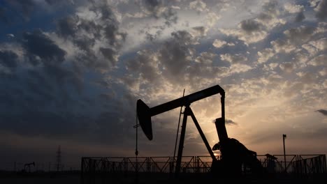 Silhouette-of-crude-oil-pump-standing-still-in-the-oilfield-at-cloudy-sunset