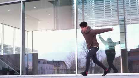 Young-parkour-athlete-doing-a-cork-in-front-of-a-glass-wall-in-slow-motion
