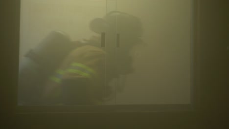 Feuerwehrleute-Rennen-An-Einem-Fenster-In-Einem-Verrauchten-Gebäude-Vorbei,-Während-Sie-Auf-Einen-Notfall-Reagieren-Und-Nach-Menschen-Suchen,-Die-Sie-Aus-Einem-Brennenden-Büro-Retten-Können