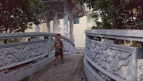 Kleiner-Junge,-Der-Auf-Der-Brücke-über-Den-Teich-Des-Buddhistischen-Tempels-In-Einem-Vorort-Von-Ho-Chi-Minh-Stadt-Vietnam-Läuft
