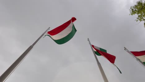 Three-Hungarian-flags-on-flagpoles-blowing-in-the-wind-with-storm-clouds-in-the-background---120-fps-slow-motion