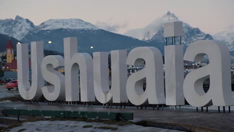 Turista-De-Tiro-Medio-Tomando-Fotos-En-El-Letrero-De-Ushuaia-Y-Montañas-En-El-Fondo