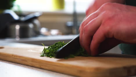 Young-male-chef-is-chopping-parsley-on-a-wooden-chopping-board,-preparing-a-vegetarian-and-vegan-meal