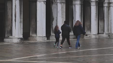 Three-people-walking-St-Mark-Square-on-rainy-day,-Venice