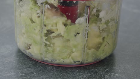 Close-up-of-an-manual-kitchen-machine-cutting-and-mixing-up-an-avocado-and-onions