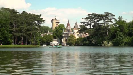 View-of-Laxenburg-castle-behind-lake-with-boats-passing-on-bright-and-sunny-summer-day
