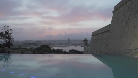 Bewölkter,-Farbenfroher-Blick-Auf-Den-Sonnenuntergang-über-Dem-Grand-Harbour-Von-Valletta,-Blick-Vom-Luxuriösen-Infinity-Pool-–-Slider-Zeitlupenaufnahme