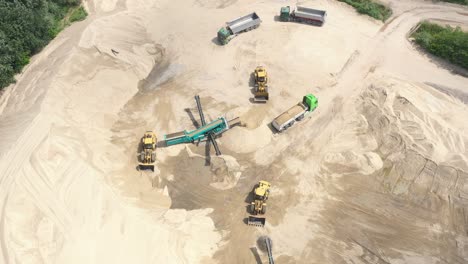 Top-aerial-view-of-bulldozer-loading-sand-into-empty-dump-truck-in-open-air-quarry