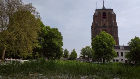 Old-Church-Tower-Oldehove-Leeuwarden-fast-dolly-shot-in-front-the-river-EE-with-moored-boats-in-the-park