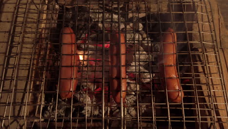 Birds-Eye-Shot-of-Sausages-on-a-Charcoal-BBQ-at-Night-Creating-Flames---Smoke-from-the-Dripping-Fat