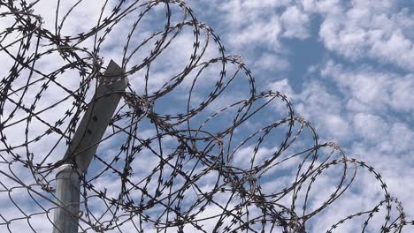 Close-Shot-of-a-Barbed-Wire-Fence-with-Fluffy-Clouds-in-the-Background