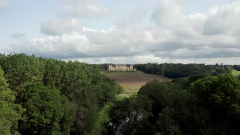 Aerial-Reveal-of-Harewood-House,-a-Country-House-in-West-Yorkshire,-through-the-Treetops