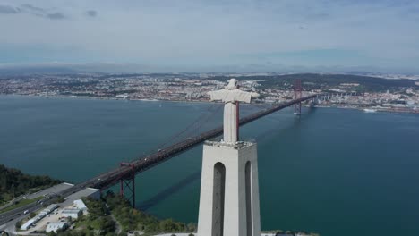Aerial-drone-shot-circling-around-Christ-the-King-Statue-and-Lisbon-Bridge-with-aeroplane-flying-in-the-background