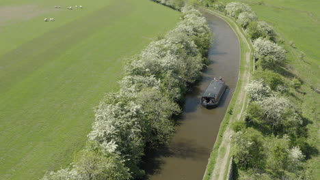 Eine-Luftaufnahme-Eines-Kanalboots,-Das-An-Einem-Sonnigen-Frühlingstag-Einen-Kanal-Hinunterfährt,-Der-Von-Der-Landschaft-Von-Yorkshire-Umgeben-Ist
