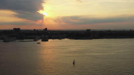 drone-ascends,-truck-right-up-to-golden-sunset-with-ferry---sailboat-on-the-Hudson-River-with-New-Jersey-in-the-background
