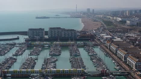 Aerial-reveal-of-Brighton-Pier,-Beach,-town---i360-attraction-from-moored-sailing-boats---yachts-in-Brighton-Marina