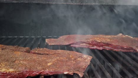 Slider-shot-seasoned-beef-navel-brisket-cooking-on-grill-of-meat-smoker