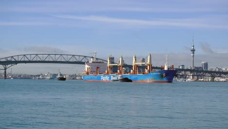 Auckland-harbor-bridge,-cargo-ship-travels-pass-harbor-bridge-with-sky-city-in-the-background