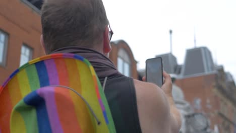 Leeds-Pride-LGBTQ-Festival-2019-Homosexuell-Bisexueller-Mann-Aufnahme-Teilen-Social-Media-Livestreaming-Pride-2019-Event-Vom-Smartphone-IPhone-Mit-Regenbogen-Pride-Hut-Outfit-4k-25p