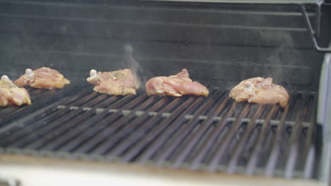 Man's-hand-using-tongs-to-place-raw-chicken-on-barbecue