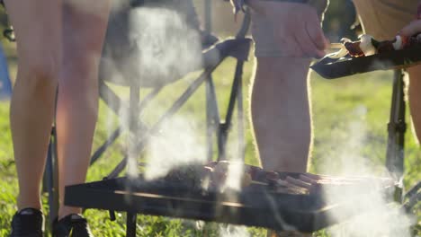 Legen-Sie-Kebab-Spieße-Auf-Einen-Offenen-Lagerfeuergrill-Mit-Dem-Lager-Im-Hintergrund