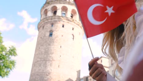 Cámara-Lenta:-Atractiva-Joven-Hermosa-Ondea-La-Bandera-Turca-Frente-A-La-Torre-De-Galata,-Un-Hito-Popular-En-Estambul,-Turquía