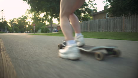 Girl's-legs-as-she-rides-longboard-at-golden-hour-down-residential-neighborhood