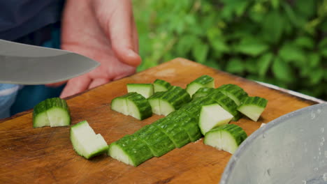Close-shot-of-man-hands-cutting-cucumber-with-a-knife-on-wooden-board