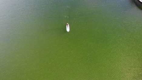 SUP-boarder-paddling-on-green-water-passing-boat-drone-footage