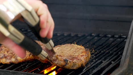 A-pair-of-tongs-flipping-a-steak-as-fire-shoots-up-from-below