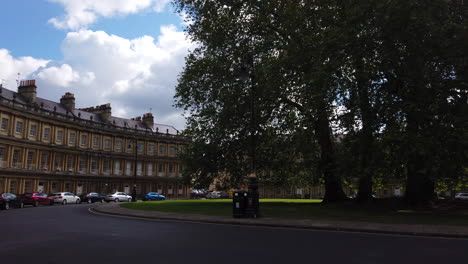 The-Circus-in-Bath,-Somerset-on-Summer’s-Day-with-Blue-Sky---White-Clouds-and-Traffic-Passing-Through-Frame-Panning-from-Left-to-Right